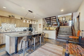 A kitchen with a central island, bar stools, a staircase, and a dining area. - Top-level condo close to summer fun with grills, hot tubs & parking (Steamboat Springs)