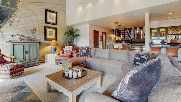 A spacious living room with a large sofa, a coffee table, and a dining area with a chandelier. - Top-level condo close to summer fun with grills, hot tubs & parking (Steamboat Springs)