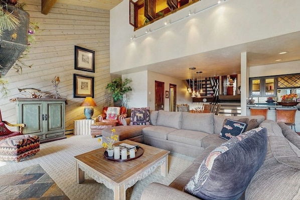 A spacious living room with a large sofa, a coffee table, and a dining area with a chandelier. - Top-level condo close to summer fun with grills, hot tubs & parking (Steamboat Springs)