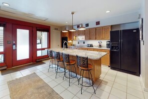 A kitchen with a central island, bar stools, wooden cabinets, and a black refrigerator. - Charming condo with large kitchen & living area - perfect for a mountain getaway (Steamboat Springs)