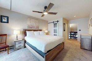 A bedroom with a bed, nightstand, chair, ceiling fan, and a door leading to another room. - Charming condo with large kitchen & living area - perfect for a mountain getaway (Steamboat Springs)