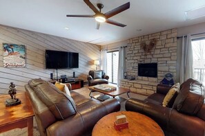 A modern living room with leather sofas, a flat-screen TV, a fireplace, and a ceiling fan. - Charming condo with large kitchen & living area - perfect for a mountain getaway (Steamboat Springs)