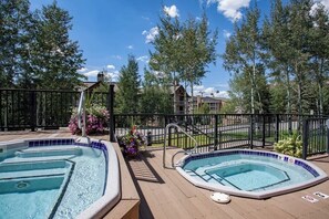 A pool area with two hot tubs, surrounded by a wooden deck and a metal fence. - Charming condo with large kitchen & living area - perfect for a mountain getaway (Steamboat Springs)