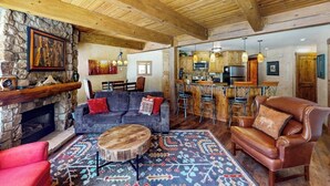 Ein rustikales Interieur mit Kamin aus Stein, einer Couch, einem Ledersessel und einer Bar.