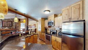 Eine Küche mit Granit Arbeitsplatten, Holzschränken, einem Edelstahlkühlschrank und einer Küchenwand mit Naturstein.
