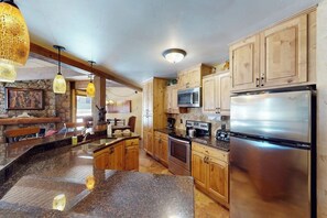 Eine Küche mit Granit Arbeitsplatten, Holzschränken, einem Edelstahlkühlschrank und einer Küchenwand mit Naturstein.