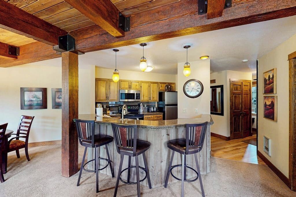 A kitchen with wooden beams, a bar area with stools, and a clock on the wall.