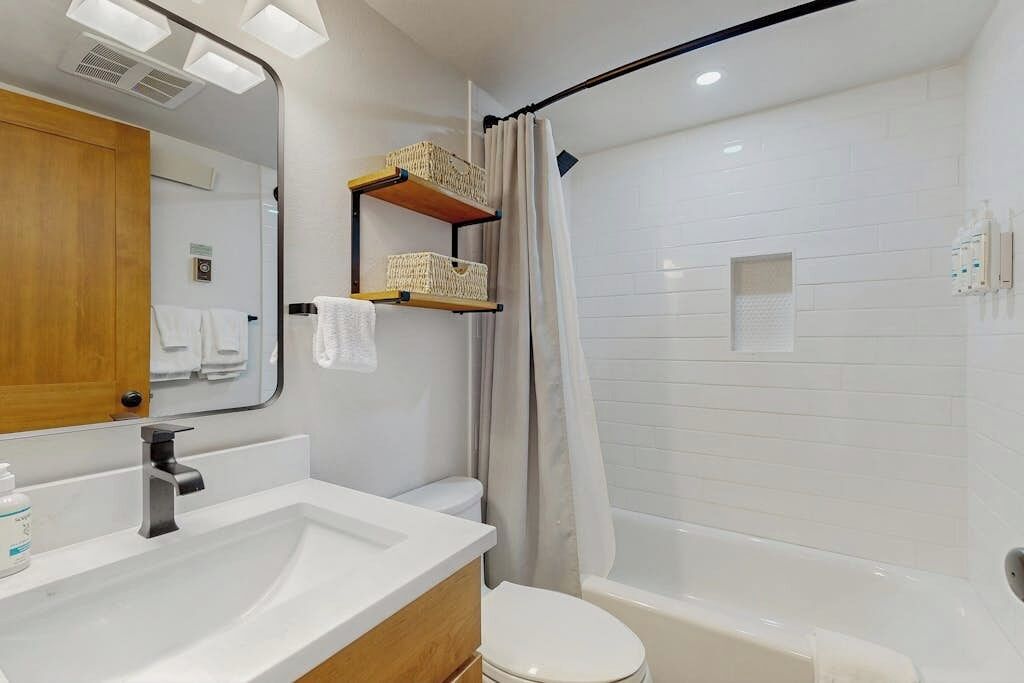 A modern bathroom with a white sink, a wooden vanity, a white toilet, and a separate shower area.