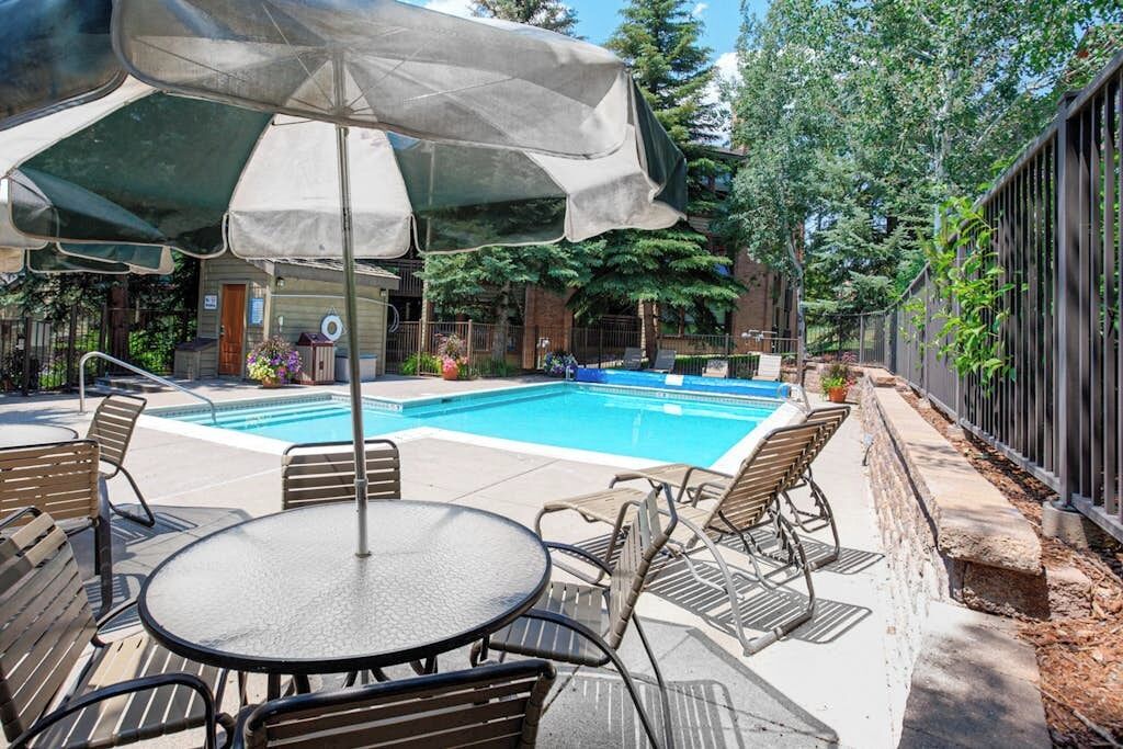A swimming pool with a patio area, including a table and chairs, and a covered umbrella.
