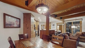 Ein Essbereich mit einem Holztisch und Stühlen, einer Chandelüster und Blick in die Küche.