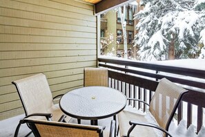 Ein überdachter Außenbereich mit rundem Tisch, zwei Stühlen, einem Holgitter und Blick auf schneebedeckte Bäume.