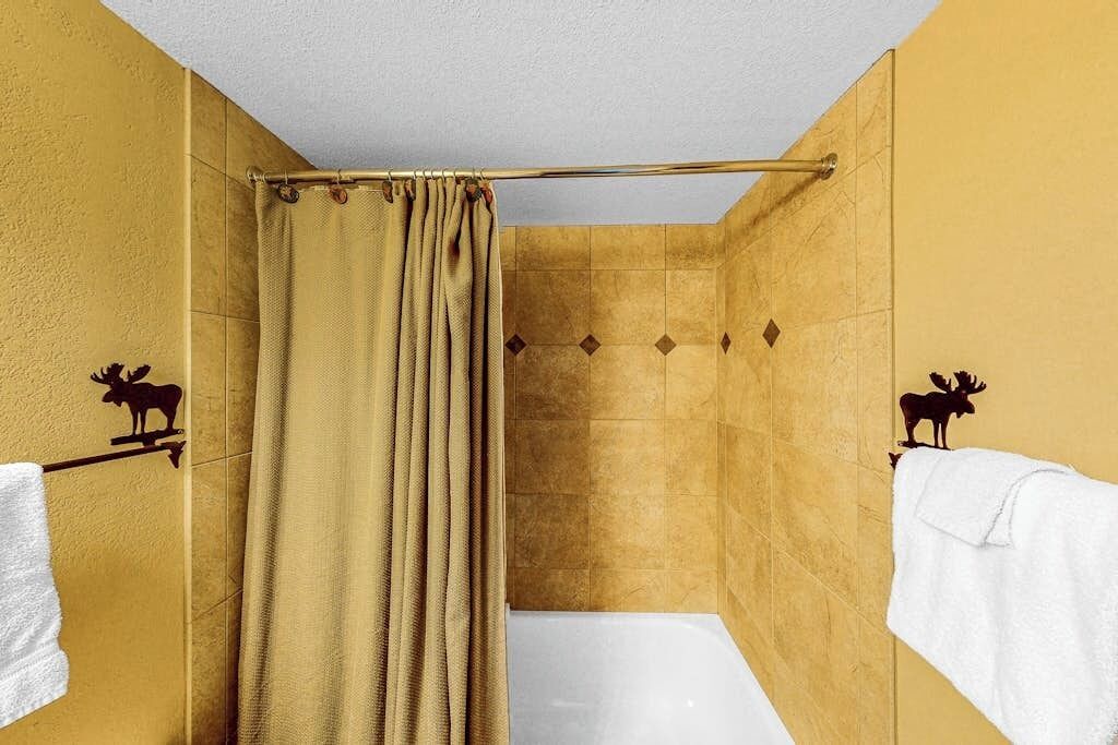 A bathroom with a shower curtain, a bathtub, and two towels hanging on towel bars with moose designs.