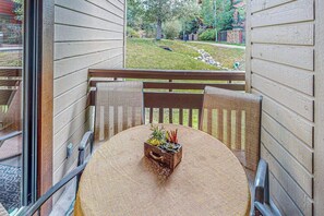 A balcony with a round table, chairs, and a small wooden box with plants.