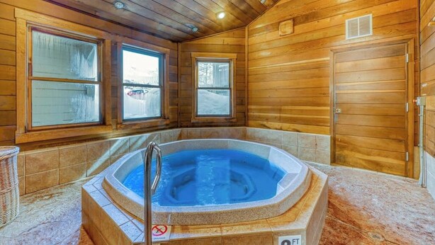 Interior de una cabaña de madera con hidromasaje, ventanas amplias y una puerta.
