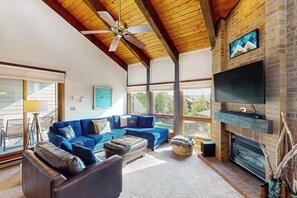 Ein großzügiges Wohnzimmer mit einem blauen Ecksofa, einem Kamin, einem Flachbildfernseher und einem Deckenventilator.