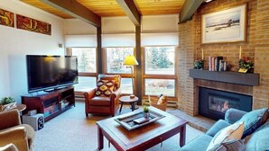 Una sala de estar con televisión, chimenea y ventanas amplias.