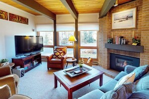 Ein Wohnzimmer mit Fernseher, Kamin und großen Fenstern.