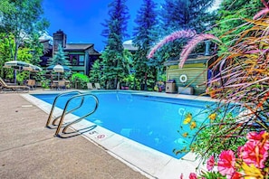 Ein Swimmingpool mit Liegestühlen und Sonnenschirmen, umgeben von Bäumen und einem Gebäude.
