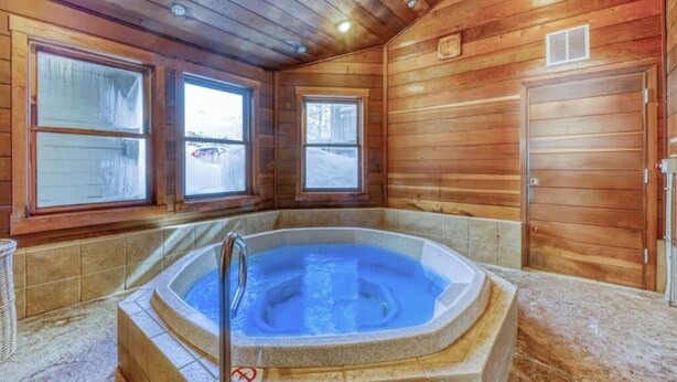 A wooden cabin interior with a hot tub, large windows, and a door. - Steamboat Springs condo with pool, hot tub & balcony (Steamboat Springs)