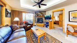 A living room with a leather sofa, a wooden coffee table, a television, and a fireplace. - Canyon Creek A105 - Family-friendly condo w/mountain views, balcony, shared hot tub & outdoor pool (Steamboat Springs)
