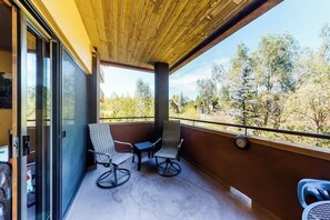 A balcony with two chairs and a table, a clock on the wall, and a view of trees. - Family-friendly condo w/mountain views, balcony, shared hot tub & outdoor pool (Steamboat Springs)