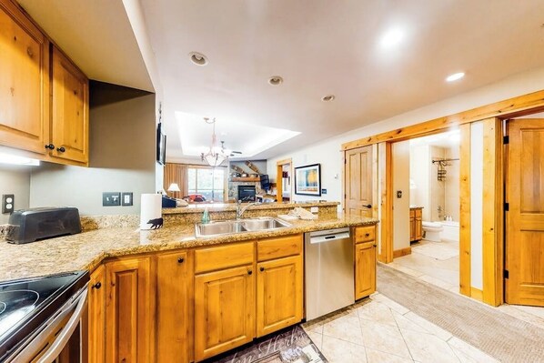A kitchen with wooden cabinets, granite countertops, a dishwasher, and a ceiling light. - Family-friendly condo w/mountain views, balcony, shared hot tub & outdoor pool (Steamboat Springs)