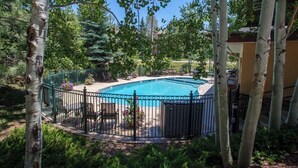 A swimming pool surrounded by a metal fence, with trees and a building in the background. - Canyon Creek A105 - Family-friendly condo w/mountain views, balcony, shared hot tub & outdoor pool (Steamboat Springs)