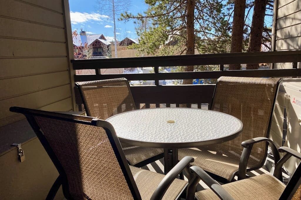 Een ronde tafel met vier stoelen, uitzicht op huizen en bomen, en een houten leuning.