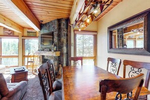 A dining area with a stone fireplace, wooden ceiling beams, and large windows. - Convenient 1st-floor Steamboat chalet with pool, hot tubs & washer/dryer (Steamboat Springs)
