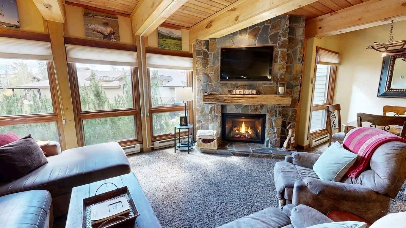 A cozy living room with a stone fireplace, comfortable seating, and large windows.