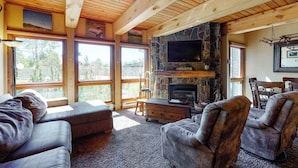 Ein geräumiges Wohnzimmer mit Kamin aus Stein, großen Fenstern und Holzboden.