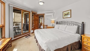 A bedroom with a bed, a nightstand, a lamp, a picture on the wall, and a sliding glass door leading to an outdoor area. - Steamboat home with washer/dryer, pools & hot tubs - near ski lifts (Steamboat Springs)