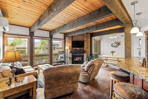 Ein gemütliches Wohnzimmer mit Kamin, Holzbalkendecke, einer Couch und einer Bar.
