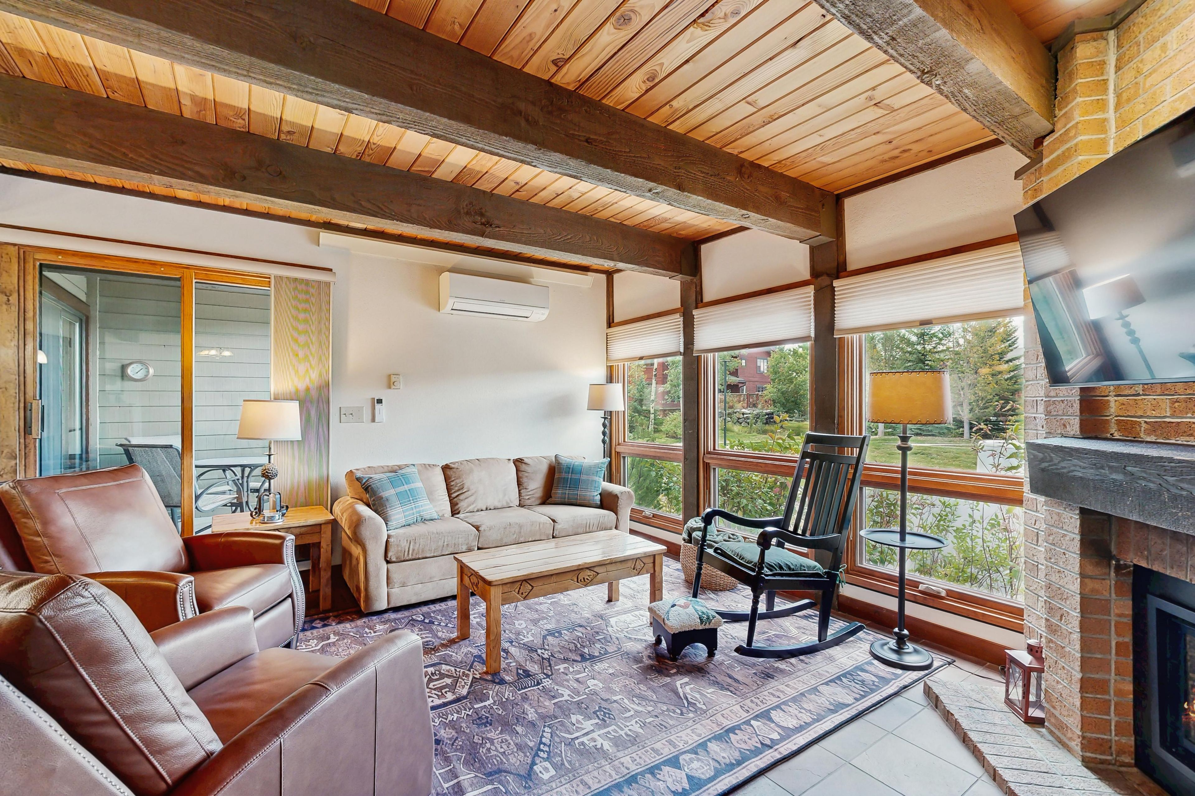 A cozy living room with a fireplace, leather furniture, and large windows offering a view of the outdoors.
