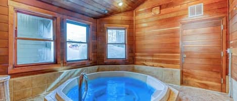 L’intérieur d’un chalet en bois, avec un jacuzzi, de grandes fenêtres et une porte.