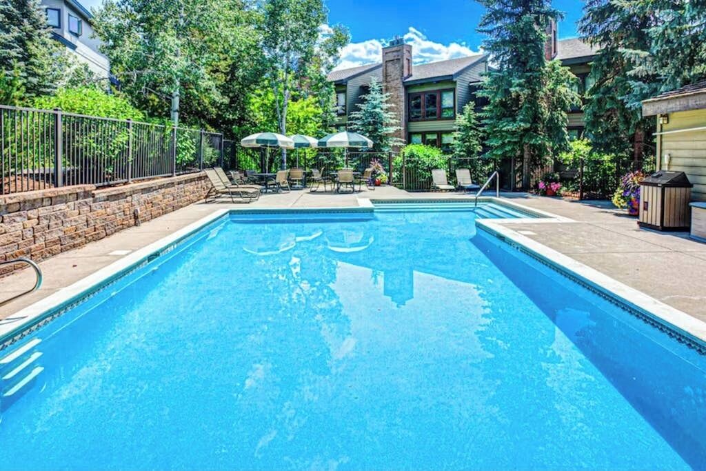 Une piscine rectangulaire avec un escalier en métal, entourée d’un mur de briques et d’une clôture en métal.