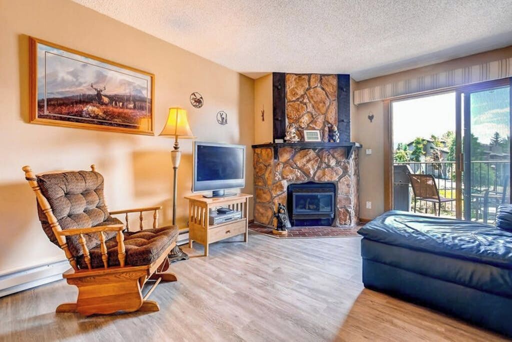 A living room with a stone fireplace, a television, a rocking chair, and a sofa.