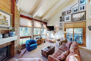 Ein Wohnzimmer mit Kamin, blauem Sessel, gemustertem Sofa und Fernseher.