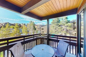 Ein Balkon mit Tisch und Stühlen, Holzbalken und Blick auf Häuser und Bäume.