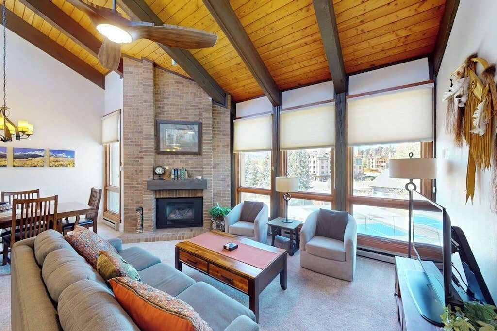 A spacious living room with a fireplace, large windows, and a view of the outside.