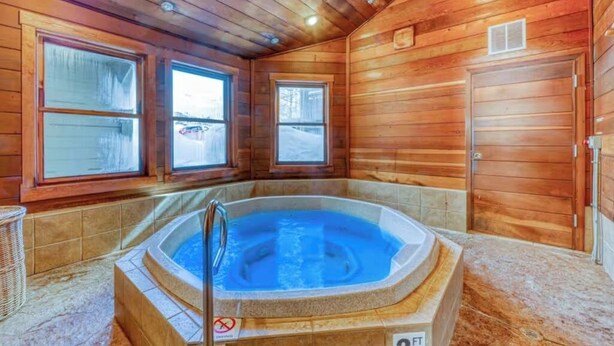 Interno di una baita in legno con vasca idromassaggio, ampie finestre e una porta.