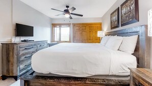 Una camera da letto con un letto, una ventola a soffitto, una TV, mobili in legno e opere d'arte alle pareti.
