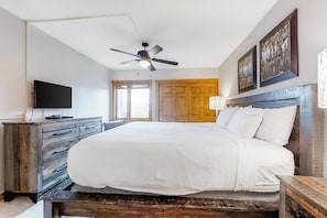 Ein Schlafzimmer mit Bett, Deckenventilator, Fernseher, Holzmöbeln und Bildern an der Wand.