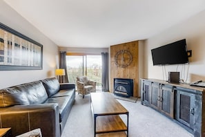 Ein Wohnzimmer mit einer Couch, einem Sessel, einem Couchtisch, einem Kamin, einem Fernseher und einer Wanduhr.