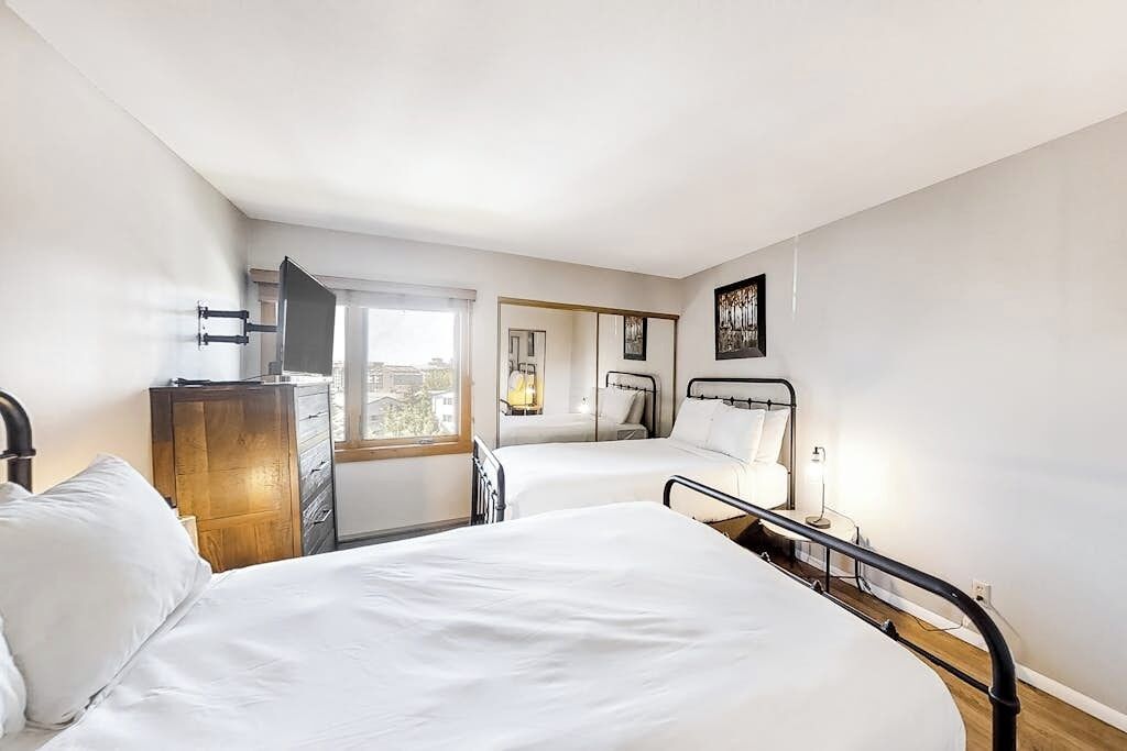 Ein Hotelzimmer mit zwei Betten, einem Holzkoffer, einem Fernseher und einem Fenster mit Blick.