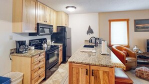 Eine kompakte Küche mit Holzausstattung, Mikrowelle, Herd, Kühlschrank, einer Arbeitsplatte aus Granit und einer kleinen Kücheninsel mit Spüle.