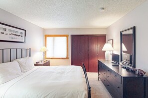 Un dormitorio con cama, lámparas de noche, cómoda, espejo y una puerta.