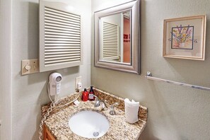 Un baño con lavamanos de encimera de granito, un espejo, un secador de pelo y una obra de arte floral enmarco.