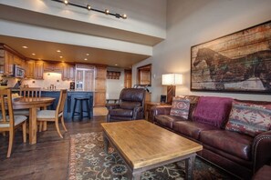 A spacious living area with a wooden coffee table, leather sofa, and a large painting. - Luxury, Top-Floor, Ski-In/Ski-Out Condo w/ Fireplace, Balcony & Shared Hot Tub (Steamboat Springs)