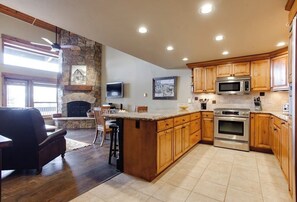 A spacious kitchen with wooden cabinets, a stone fireplace, a large island, and a built-in oven. - Luxury, Top-Floor, Ski-In/Ski-Out Condo w/ Fireplace, Balcony & Shared Hot Tub (Steamboat Springs)